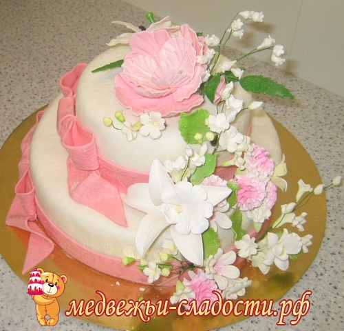 Двухъярусный белый свадебный торт с букетом из лилий, орхидей с розовыми бантами